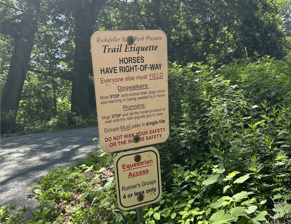 A sign at Rockefeller State Park Preserve, part of New York State Parks, outlines trail etiquette: horses have right-of-way and others must yield. It details rules for dog walkers, runners, and groups, promoting harmony and finding inner peace on the trails.